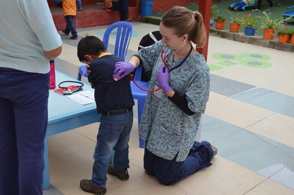 Max Niv Peru A woman in medical scrubs listens to a young boy's back with her stethoscope.